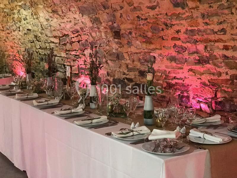 Table de réception élégamment dressée avec nappes blanches, vaisselle raffinée et décoration florale, devant un mur en…