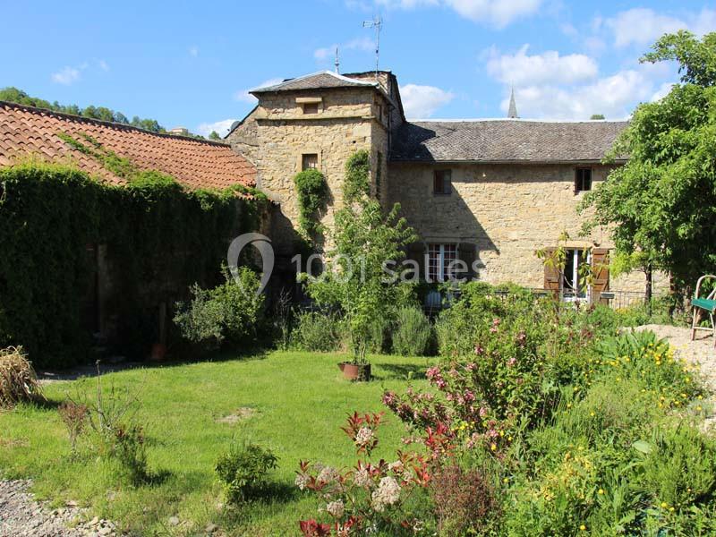 Maison en pierre ancienne entourée d'un jardin verdoyant avec des fleurs et des arbustes sous un ciel bleu.