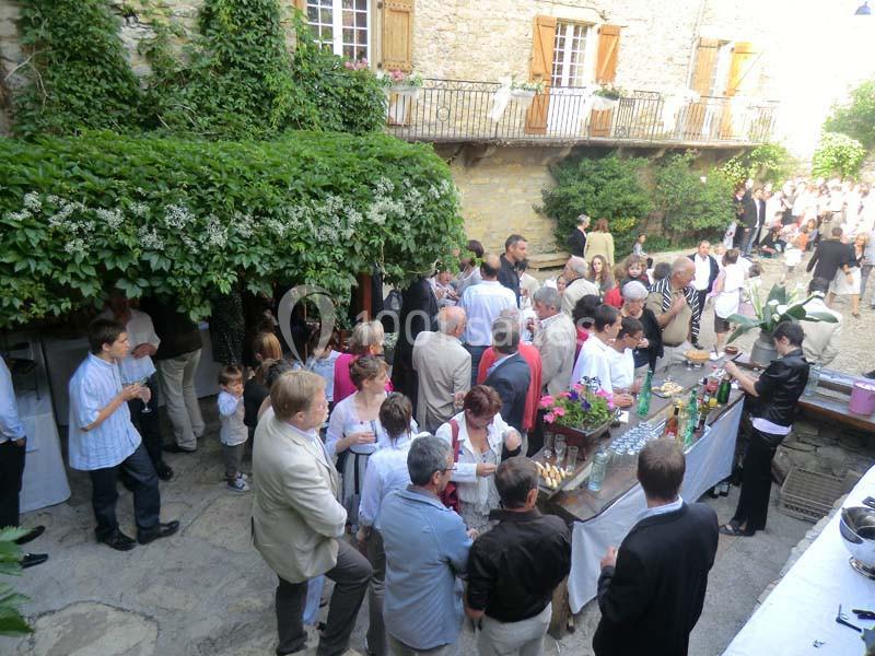 Groupe de personnes réunies dans une cour en pierre, discutant et partageant un buffet en plein air.