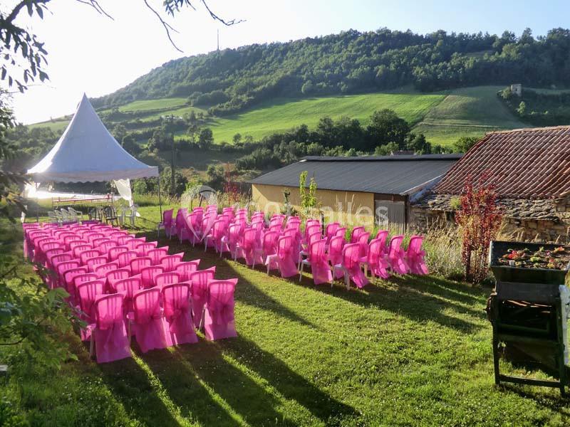 Chaises roses alignées en extérieur sur une pelouse, face à une tente blanche, avec des collines verdoyantes en arrière-plan.