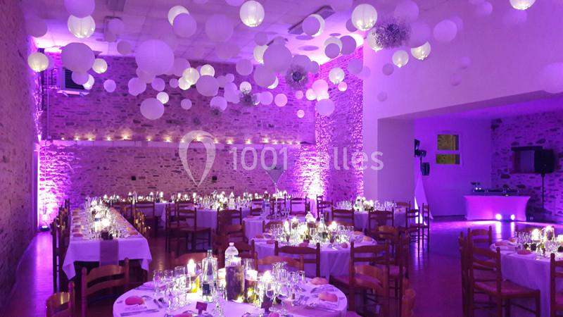 Salle de réception décorée avec des guirlandes lumineuses, des lanternes suspendues et des tables dressées pour un événement.