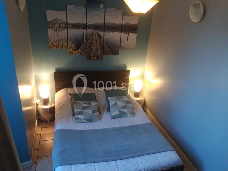 Lit double avec coussins géométriques, couverture bleue et lampes de chevet allumées dans une chambre aux murs bleus.