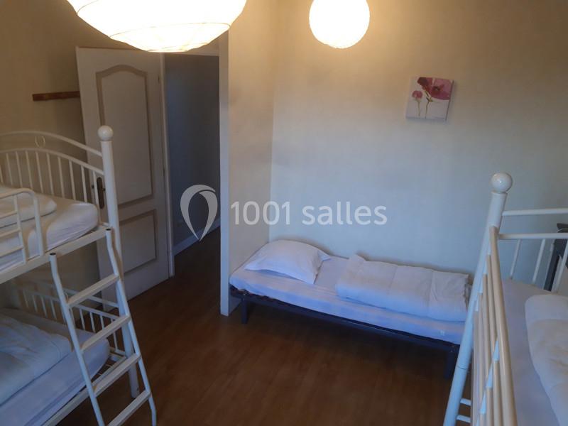 Chambre avec lits superposés et lit simple, parquet au sol, murs clairs et décoration minimaliste.