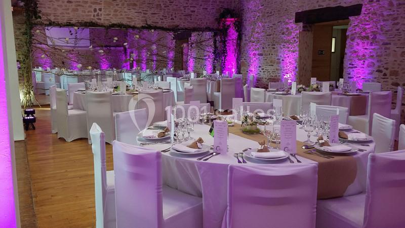 Salle de réception décorée avec des tables rondes dressées, nappes blanches et éclairage d'ambiance violet.