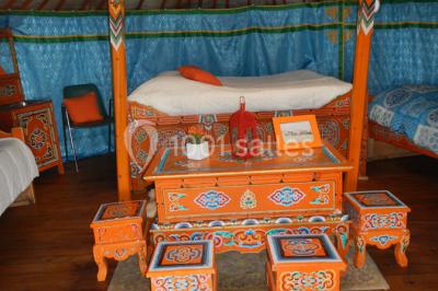 Intérieur d'un chalet en bois avec table, chaises recouvertes de fourrure, poêle allumé et vase de fleurs sur une table…