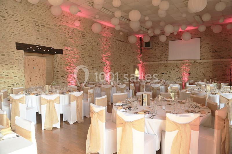 Salle de réception en pierre avec tables décorées de nappes blanches et nœuds beige, éclairage rose tamisé.