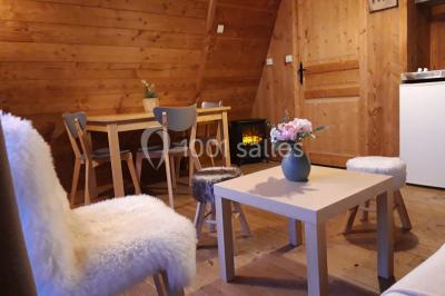 Intérieur d'un chalet en bois avec table, chaises recouvertes de fourrure, poêle allumé et vase de fleurs sur une table…