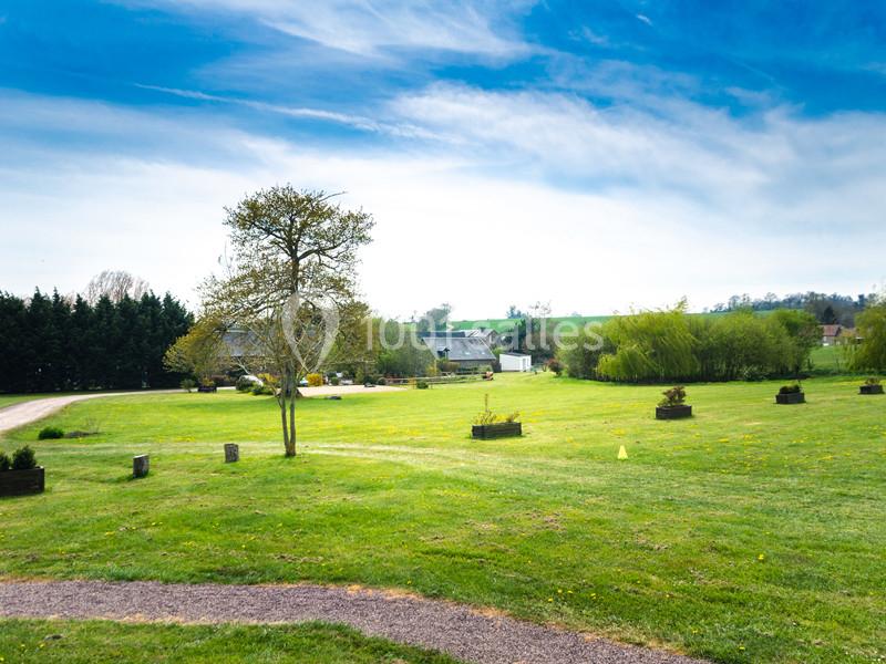 Grand espace vert avec pelouses, arbres, petites plantations et bâtiments ruraux en arrière-plan sous un ciel dégagé.