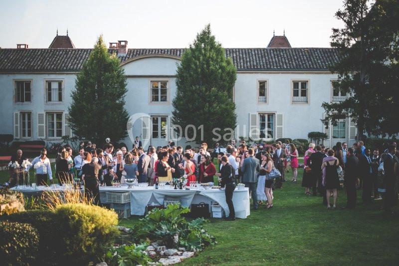 Groupe de personnes réunies dans un jardin devant un grand bâtiment, avec des tables dressées pour un événement.