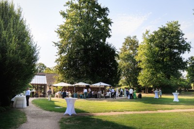 Des invités assis en plein air applaudissent lors d'une cérémonie sous des arbres aux feuilles partiellement jaunies.