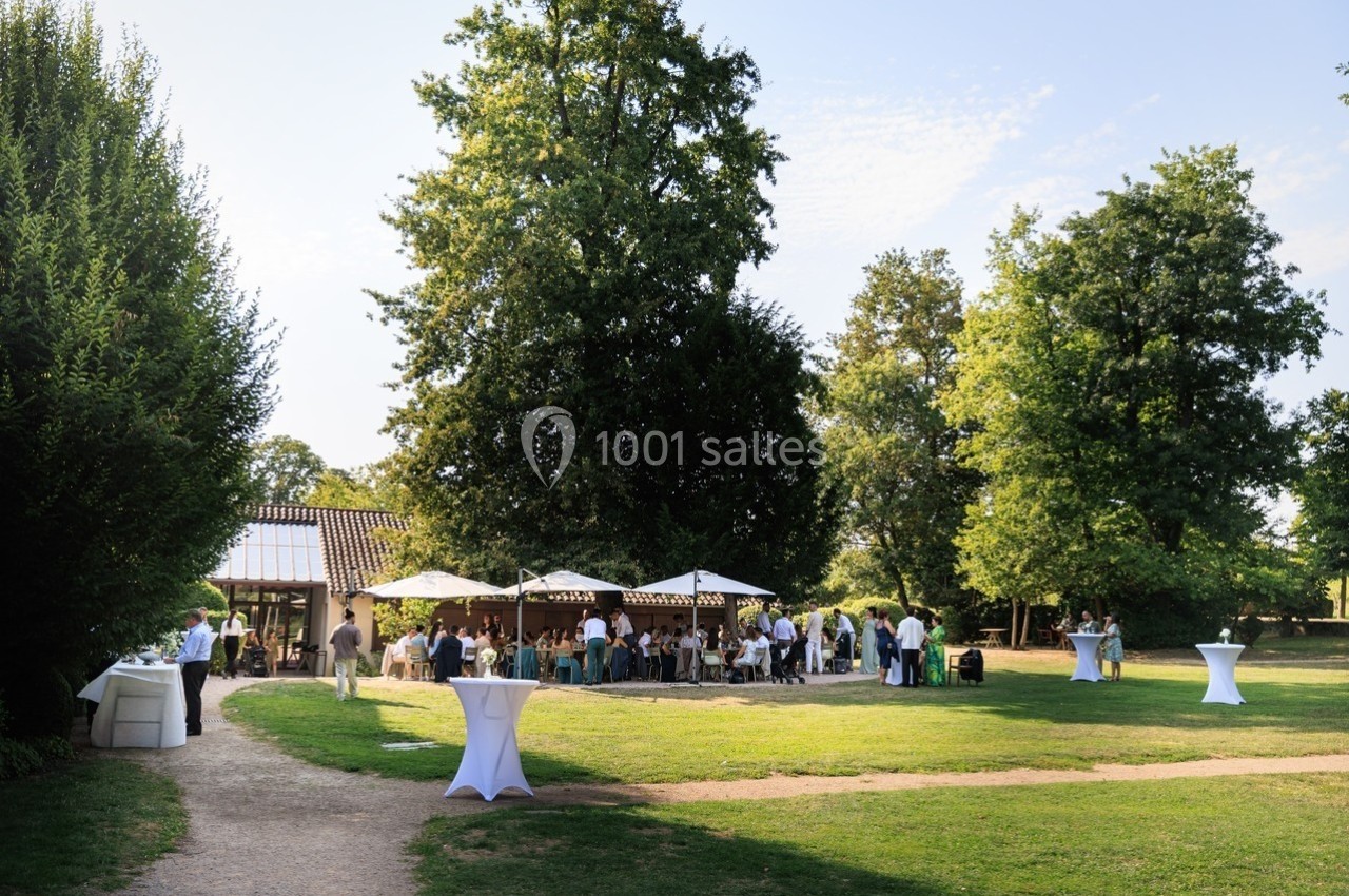 Groupe de personnes réunies dans un jardin avec tables, parasols et arbres en arrière-plan par une journée ensoleillée.