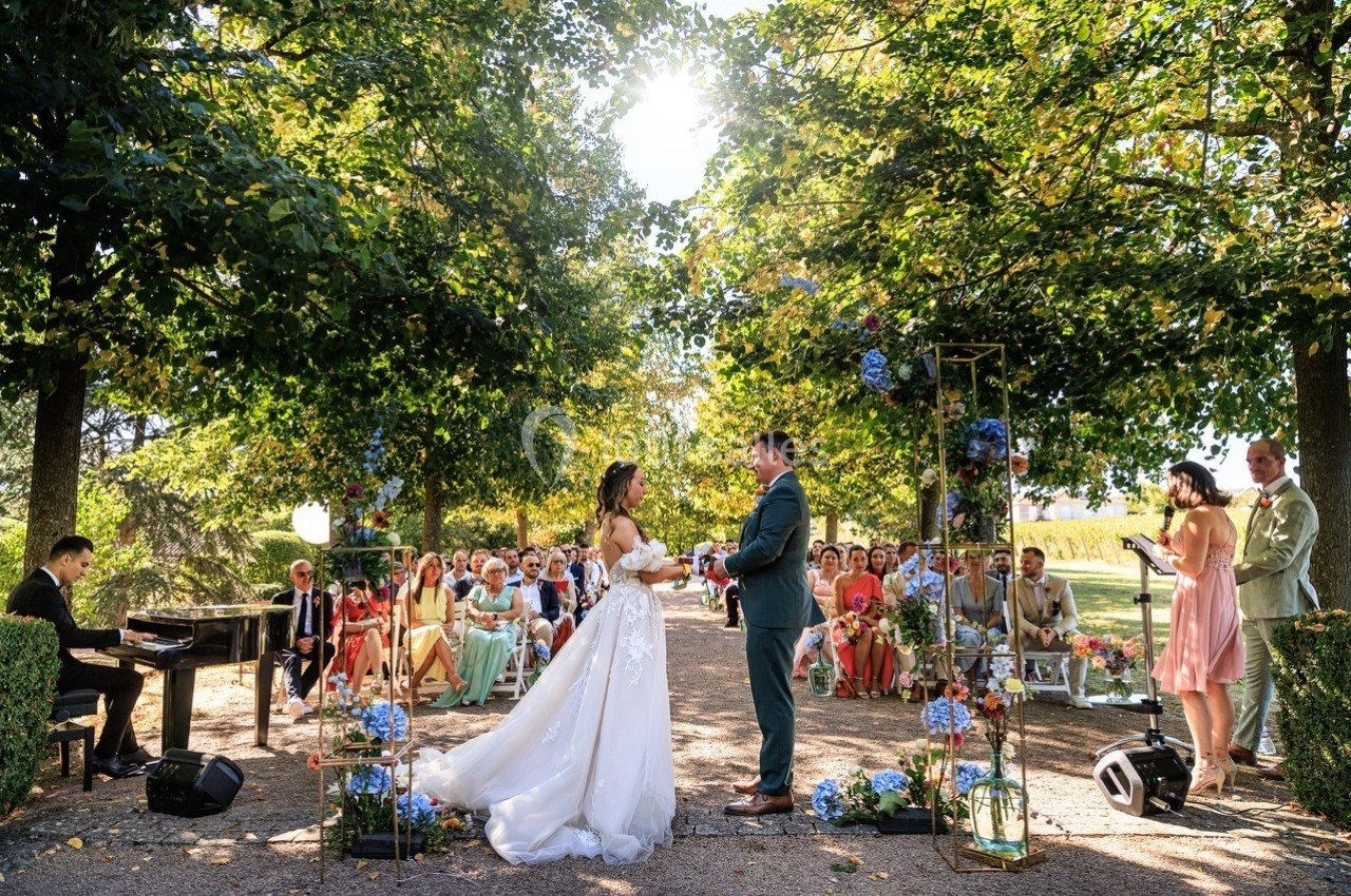 Mariage en plein air avec un couple échangeant leurs vœux devant des invités assis sous des arbres verdoyants.