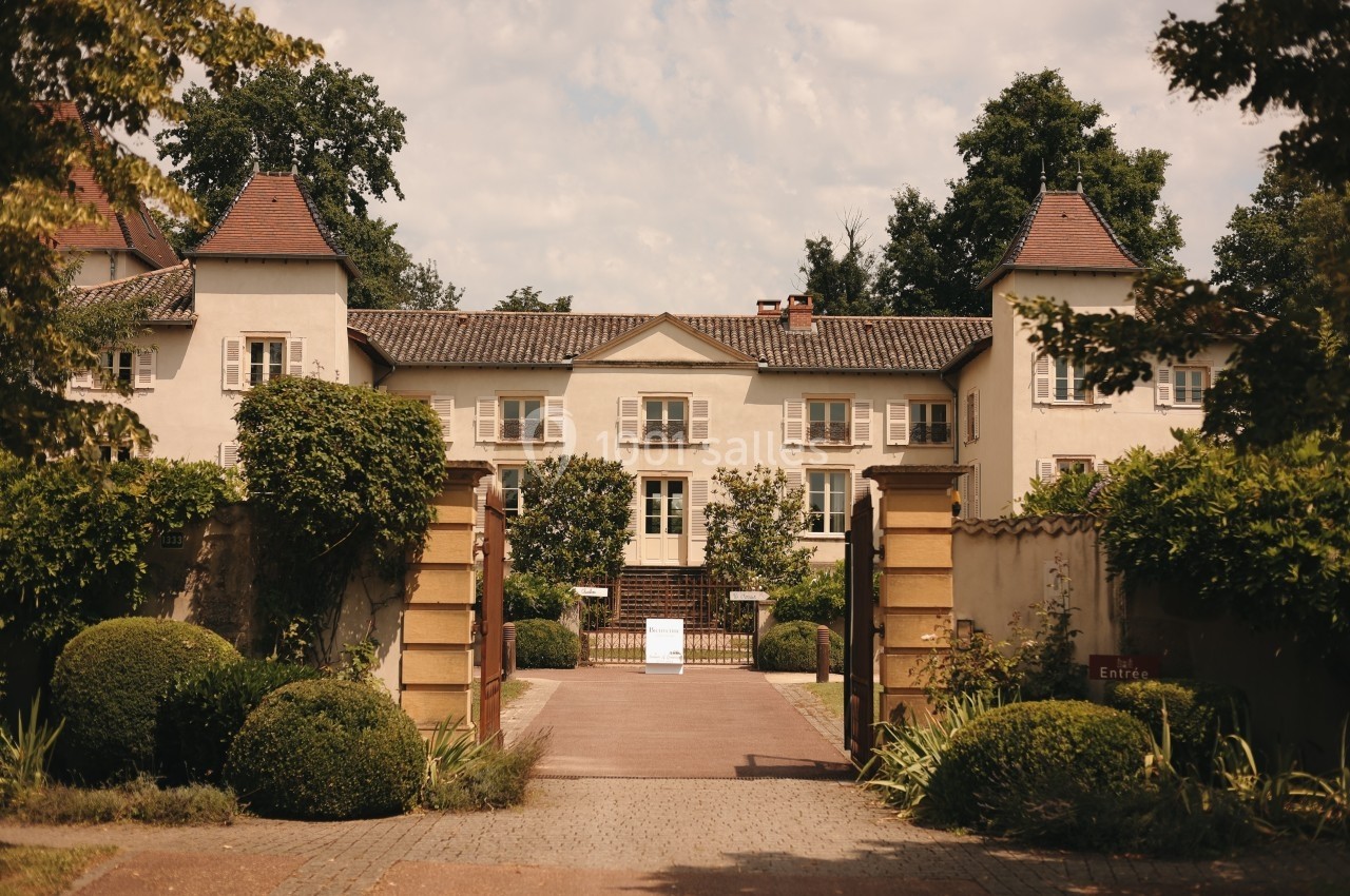 Façade d'un manoir entouré de verdure, avec une allée centrale menant à une entrée principale.