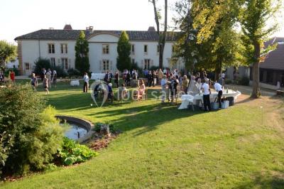 Des invités assis en plein air applaudissent lors d'une cérémonie sous des arbres aux feuilles partiellement jaunies.