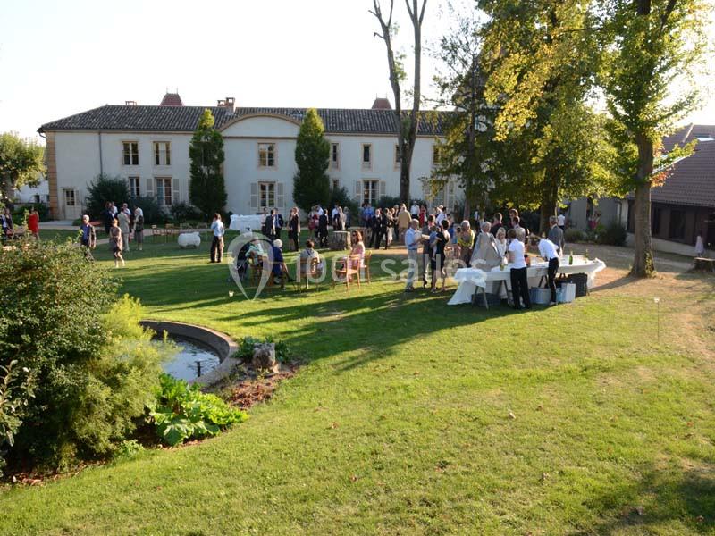 Groupe de personnes réunies dans un jardin verdoyant devant un grand bâtiment ancien par une journée ensoleillée.