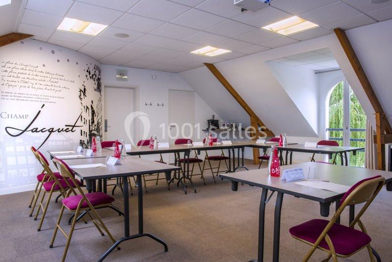 Salle de réunion lumineuse avec tables disposées en U, chaises rouges et coin café en arrière-plan.