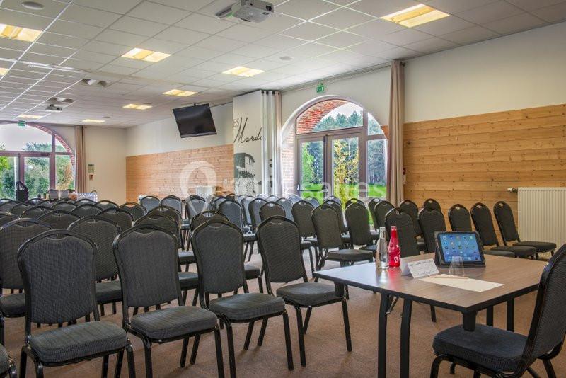 Salle de conférence lumineuse avec des rangées de chaises noires, une table équipée d'une tablette et une vue sur l…