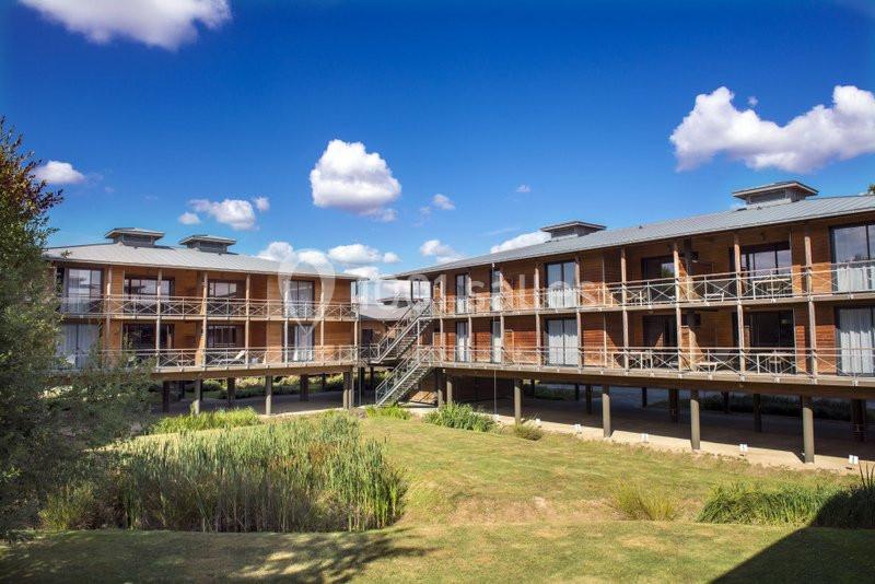 Bâtiments en bois sur pilotis entourés de végétation, sous un ciel bleu parsemé de nuages.