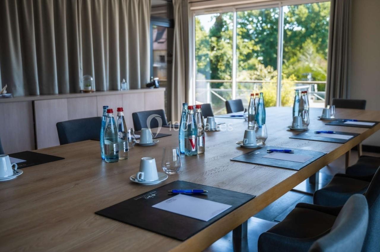 Salle de réunion lumineuse avec une grande table en bois, des bouteilles d'eau, des tasses et des blocs-notes disposés.
