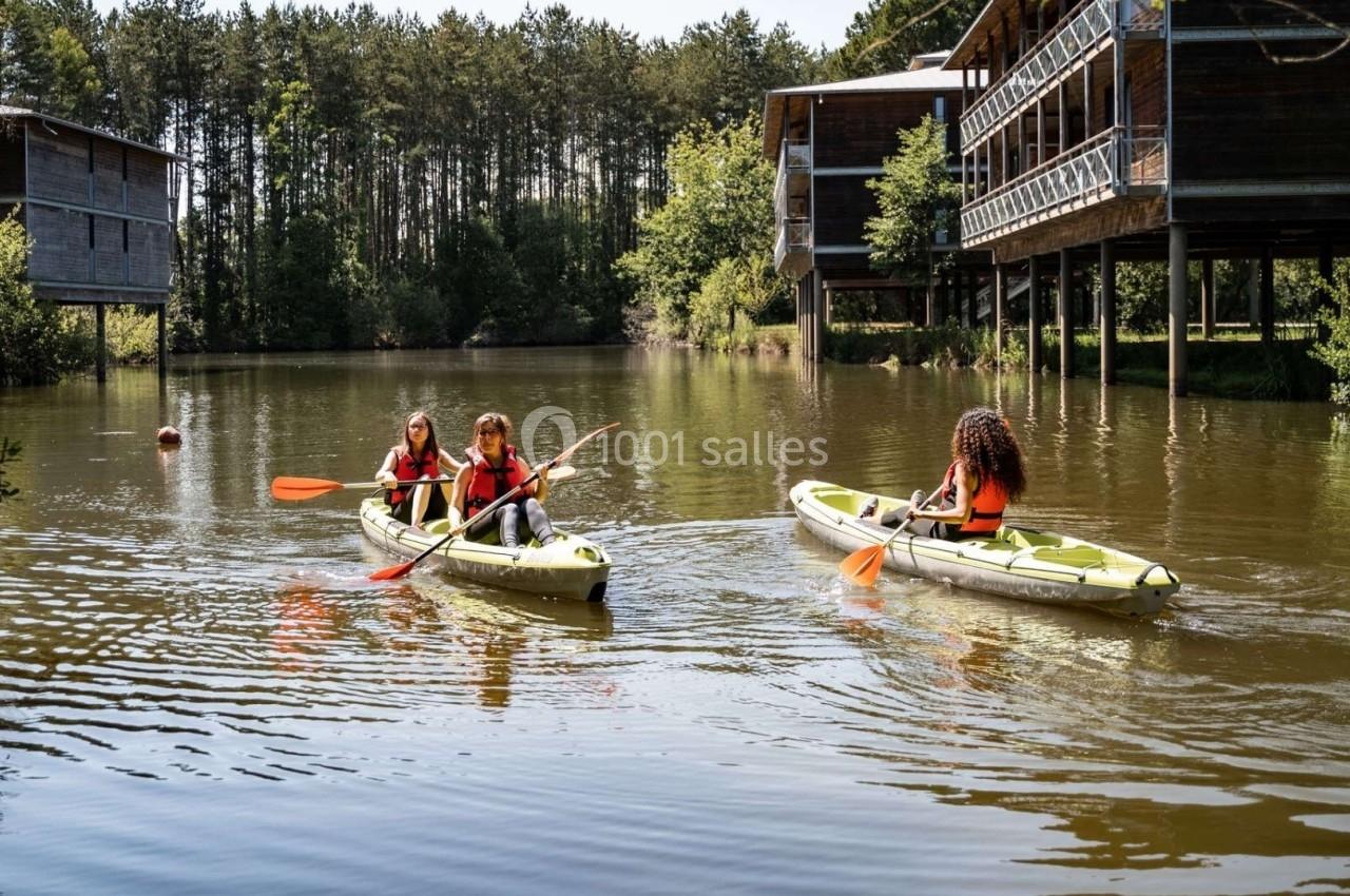 Trois personnes pagayant en kayak sur un lac entouré de cabanes en bois et d'arbres.
