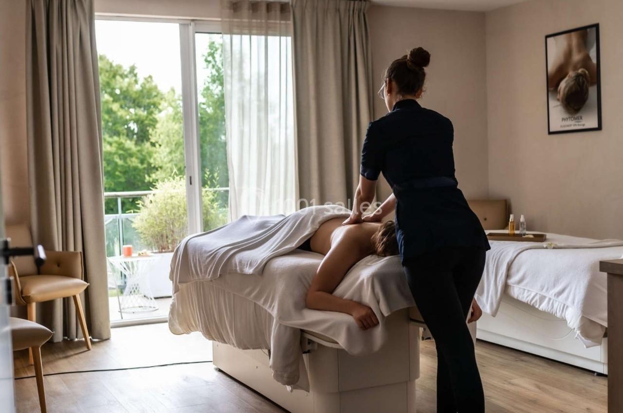 Une masseuse effectue un massage du dos dans une pièce lumineuse avec vue sur un jardin.
