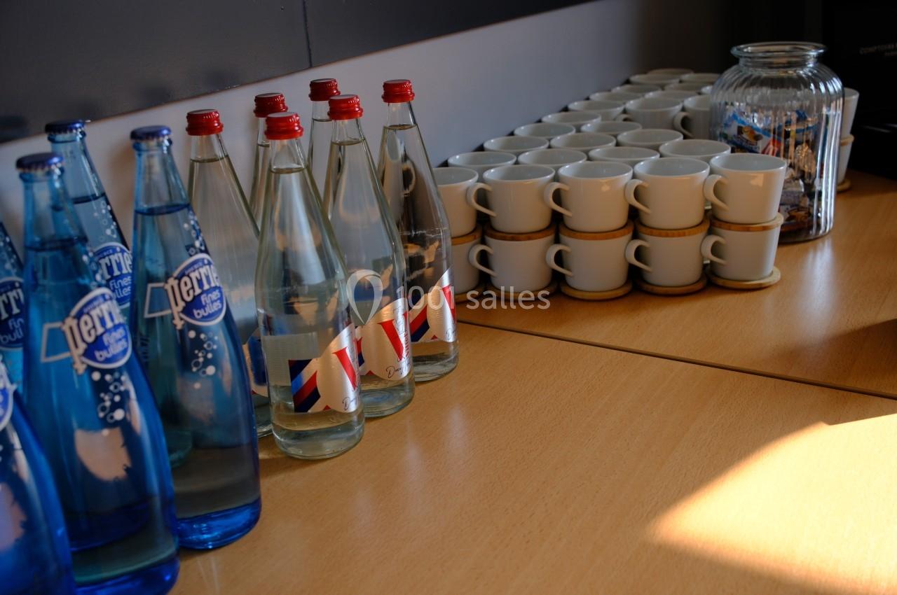 Bouteilles d'eau, tasses empilées et bocal de biscuits disposés sur une table en bois.