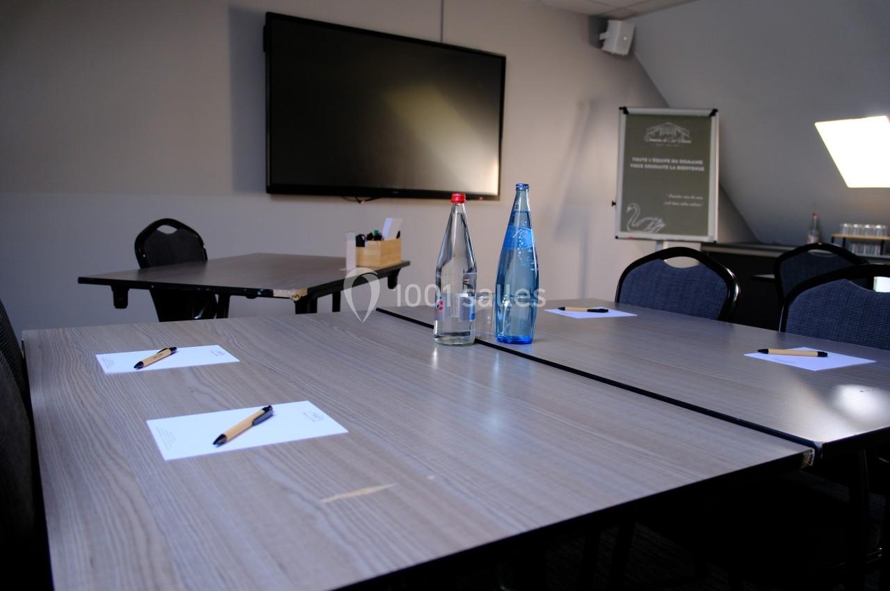 Salle de réunion avec tables en bois, bouteilles d'eau, stylos et blocs-notes, écran mural en arrière-plan.