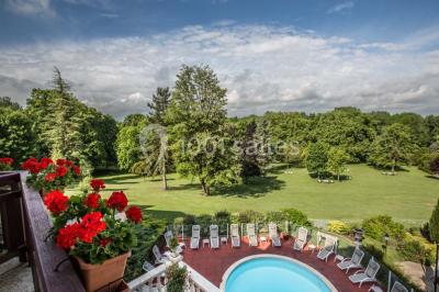 Chambre lumineuse avec parquet en bois, lit double, canapé rouge, table basse et grandes fenêtres avec rideaux fleuris.