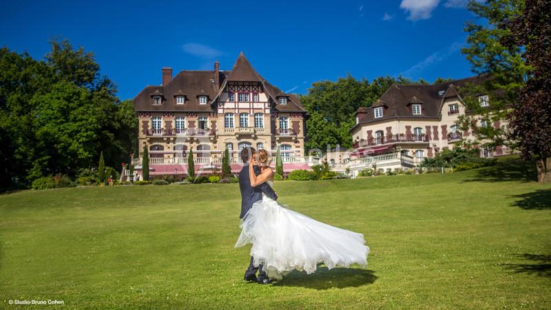 Un couple en tenue de mariage danse sur une pelouse devant un grand bâtiment de style traditionnel.