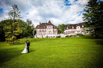 Chambre lumineuse avec parquet en bois, lit double, canapé rouge, table basse et grandes fenêtres avec rideaux fleuris.