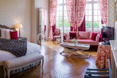 Chambre lumineuse avec parquet en bois, lit double, canapé rouge, table basse et grandes fenêtres avec rideaux fleuris.