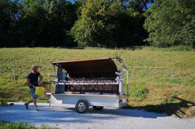 Grande maison en pierre entourée de verdure, avec une cour ensoleillée et des arbres en arrière-plan.