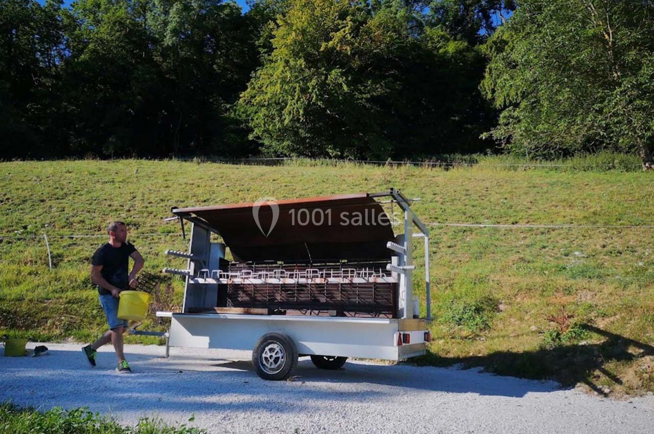 Un homme transporte un seau près d'une remorque équipée de ruches, dans un paysage verdoyant.