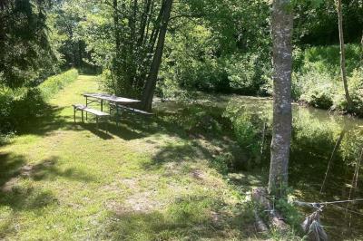 Grande maison en pierre entourée de verdure, avec une cour ensoleillée et des arbres en arrière-plan.