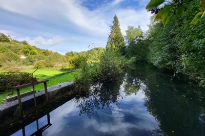 Grande maison en pierre entourée de verdure, avec une cour ensoleillée et des arbres en arrière-plan.
