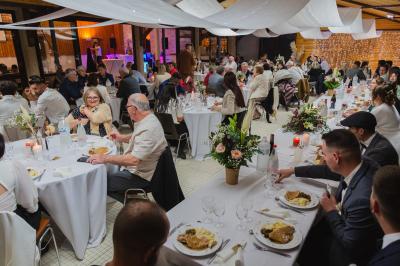Grande maison en pierre entourée de verdure, avec une cour ensoleillée et des arbres en arrière-plan.