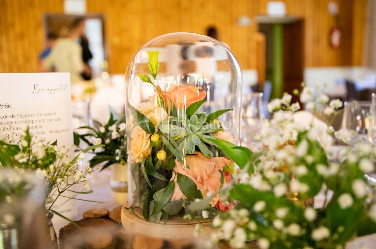 Composition florale sous cloche en verre, entourée de décorations de table et de menus dans une salle en bois.