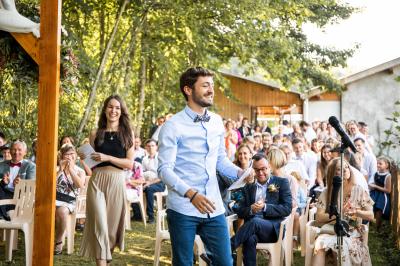 Grande maison en pierre entourée de verdure, avec une cour ensoleillée et des arbres en arrière-plan.