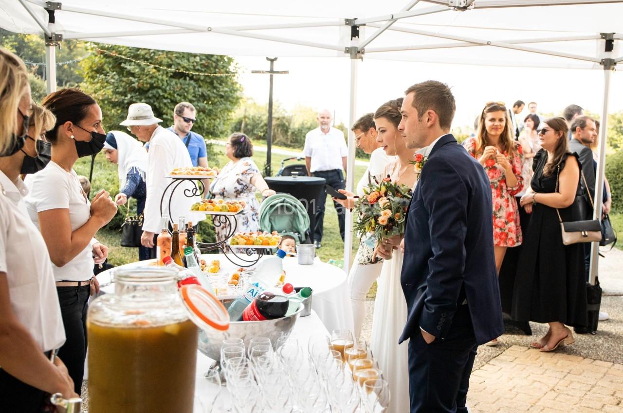 Un couple de mariés se tient devant un buffet en extérieur, entouré d'invités et de serveurs sous une tente blanche.