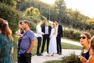 Grande maison en pierre entourée de verdure, avec une cour ensoleillée et des arbres en arrière-plan.
