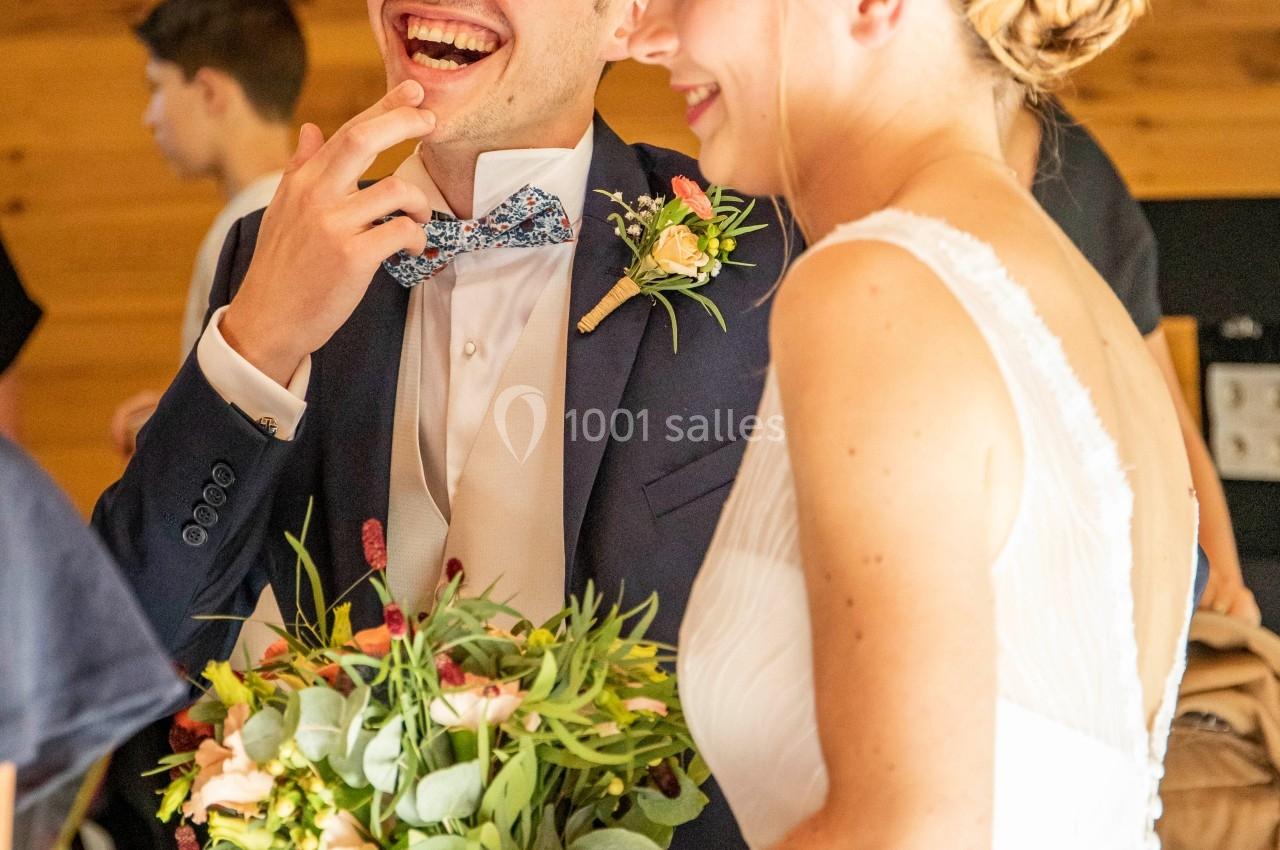 Un couple habillé pour un mariage, souriant, la mariée tenant un bouquet de fleurs.