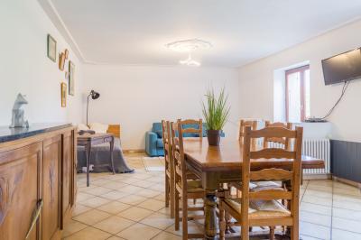 Grande maison en pierre entourée de verdure, avec une cour ensoleillée et des arbres en arrière-plan.