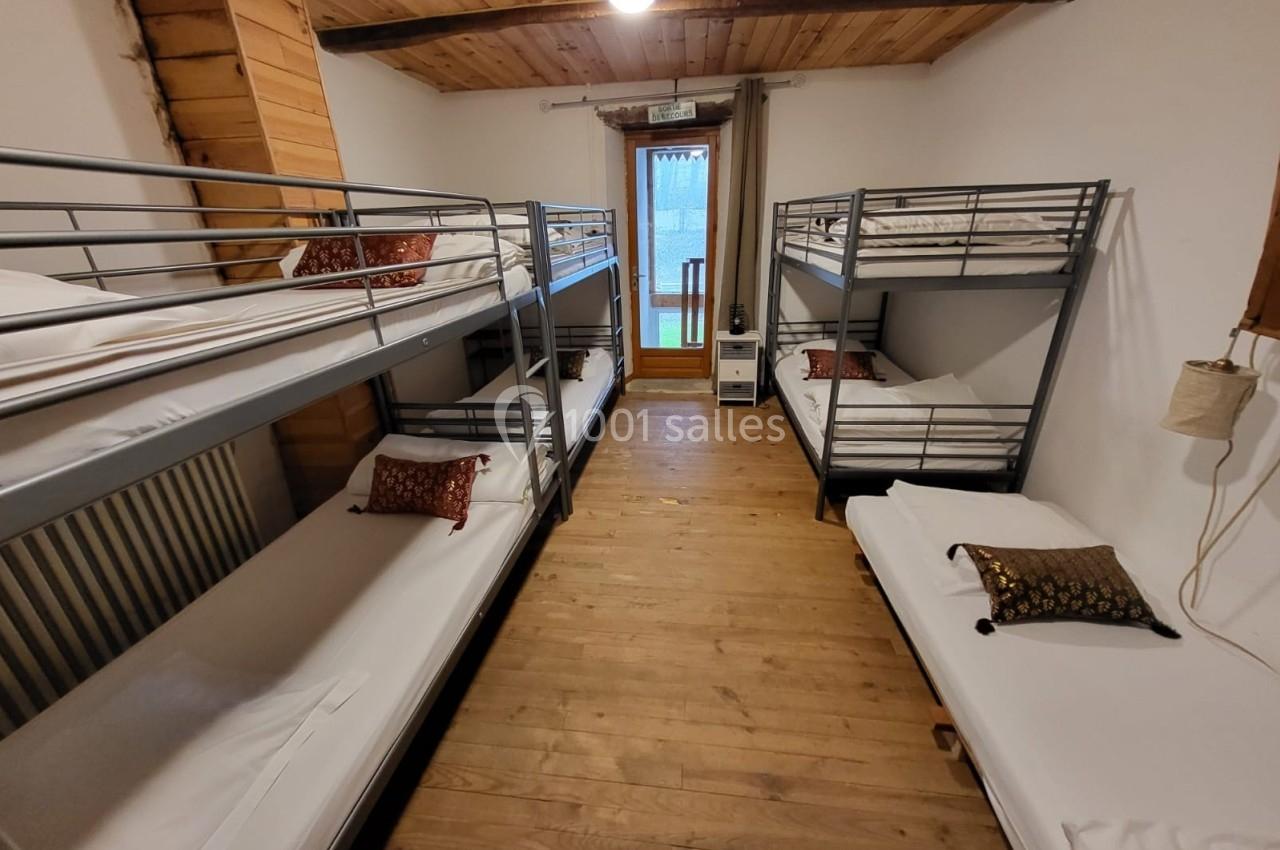 Dortoir avec lits superposés en métal, parquet en bois, plafond lambrissé et accès à un balcon lumineux.