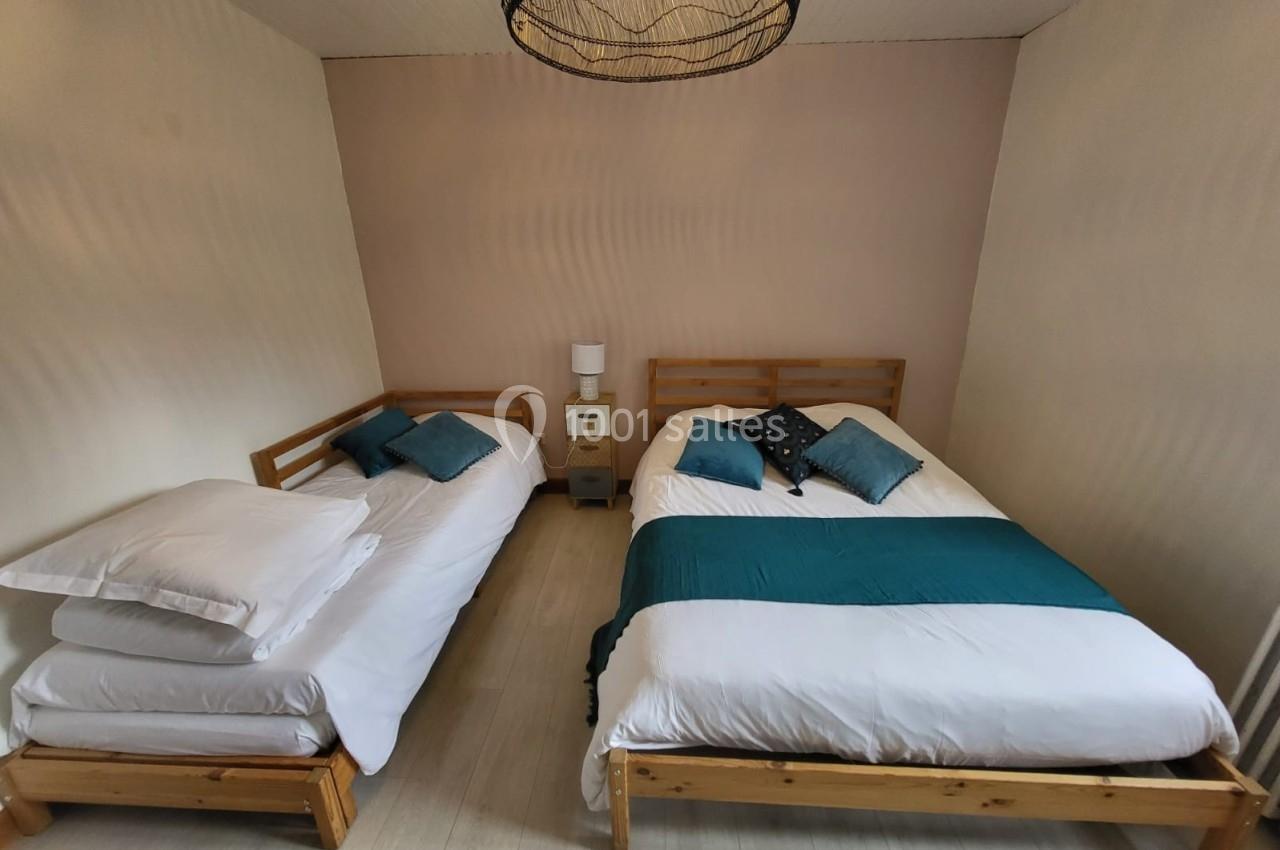 Deux lits en bois avec literie blanche et coussins bleus dans une chambre lumineuse au sol clair.