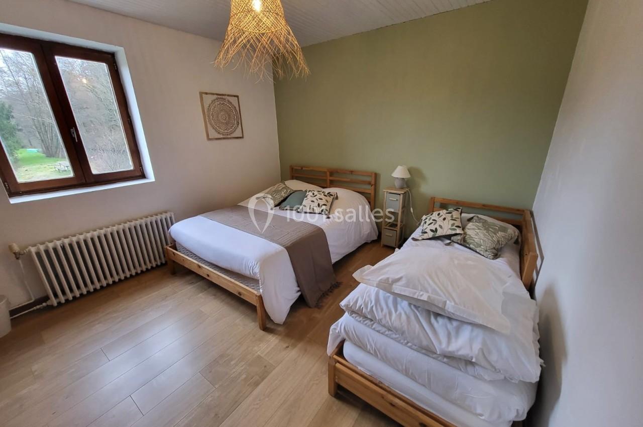 Chambre avec deux lits en bois, parquet clair, mur vert, fenêtre donnant sur un extérieur arboré.