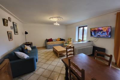 Grande maison en pierre entourée de verdure, avec une cour ensoleillée et des arbres en arrière-plan.