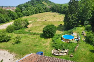 Grande maison en pierre entourée de verdure, avec une cour ensoleillée et des arbres en arrière-plan.