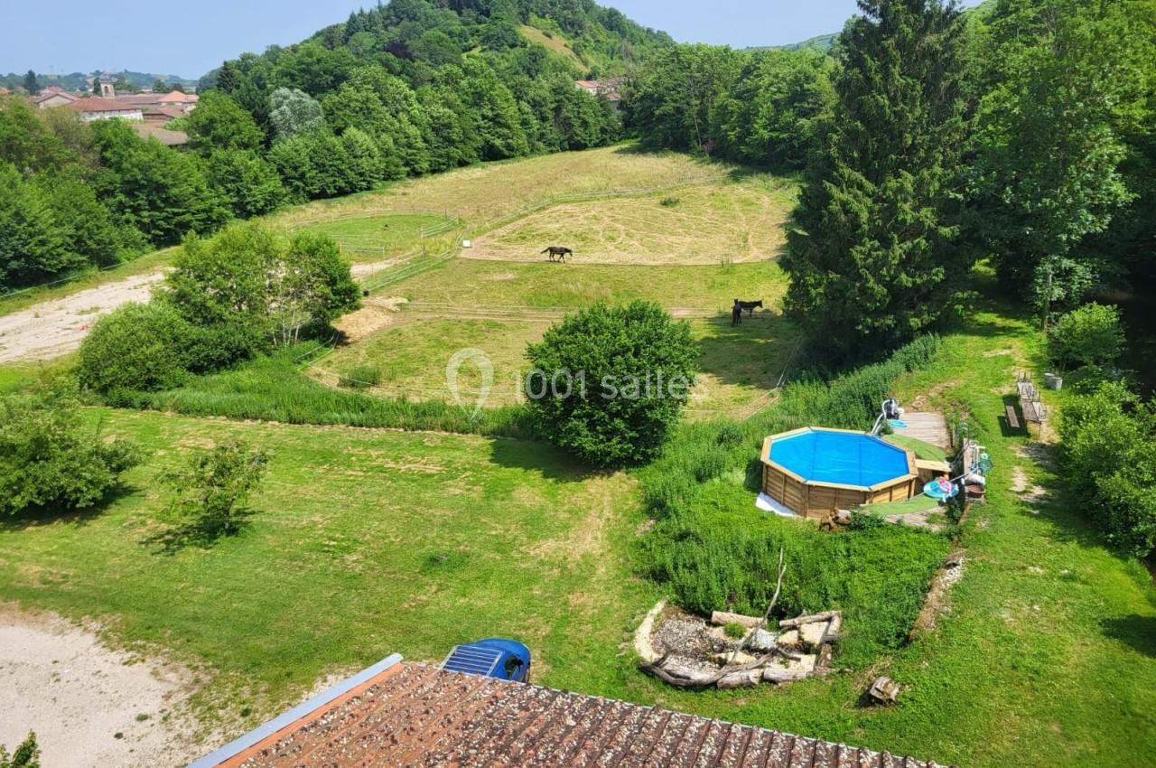 Vue aérienne d'un jardin avec une piscine hors-sol, des pâturages, des chevaux et une colline boisée en arrière-plan.