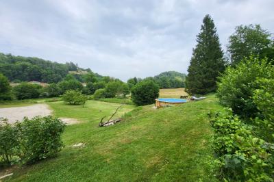Grande maison en pierre entourée de verdure, avec une cour ensoleillée et des arbres en arrière-plan.