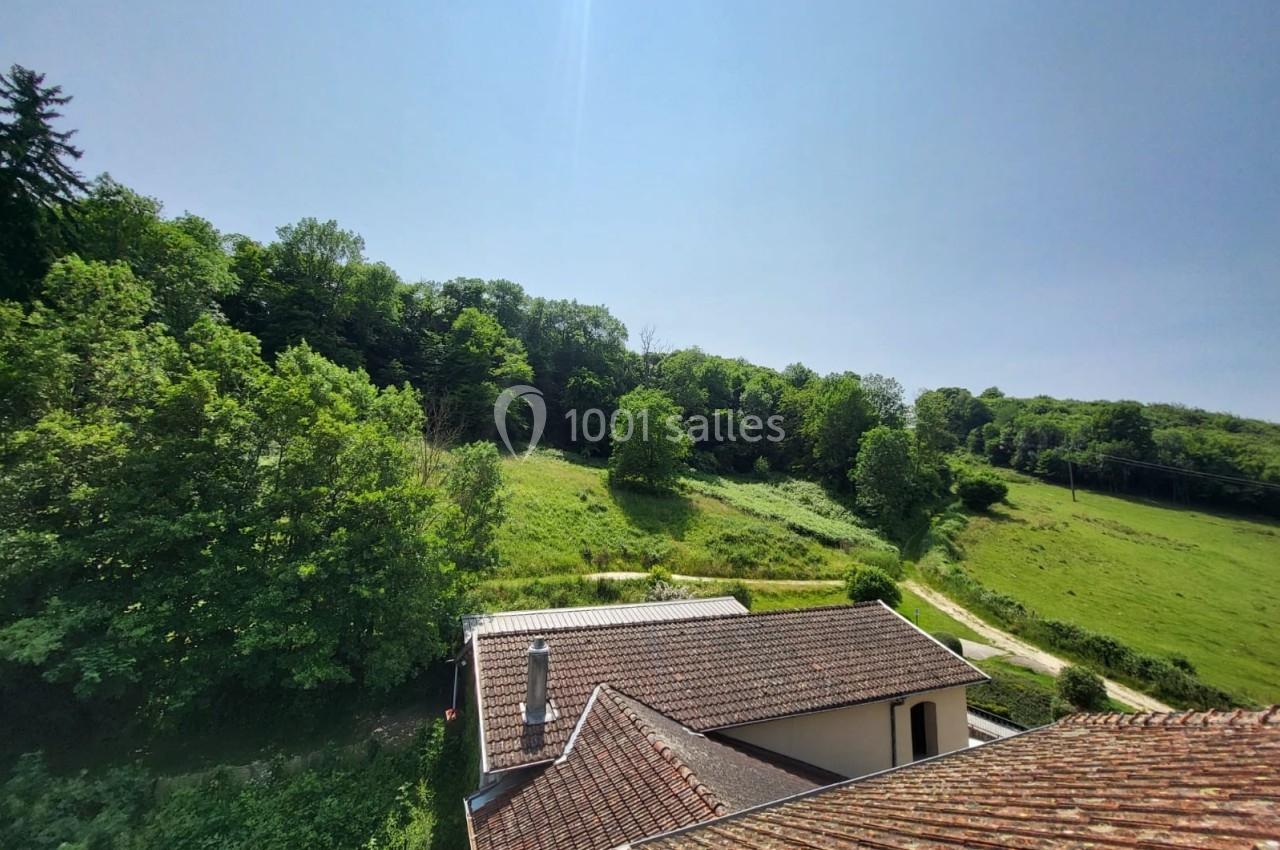 Vue depuis un toit montrant une maison, un jardin verdoyant et une colline boisée sous un ciel dégagé.